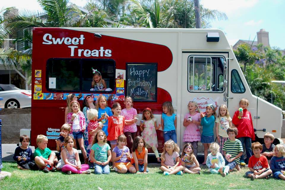 A large group of children smiling in front of a hired Sweet Treats dessert food truck.