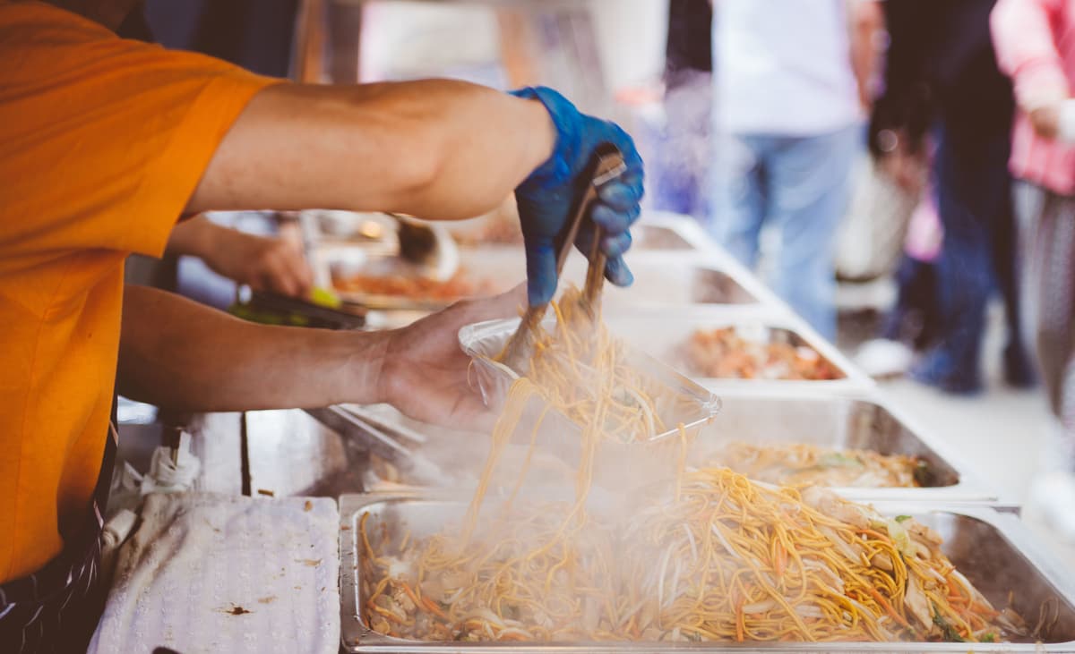 Food trucks over traditional catering where a vendor is serving fresh noodles at an outdoor catering event