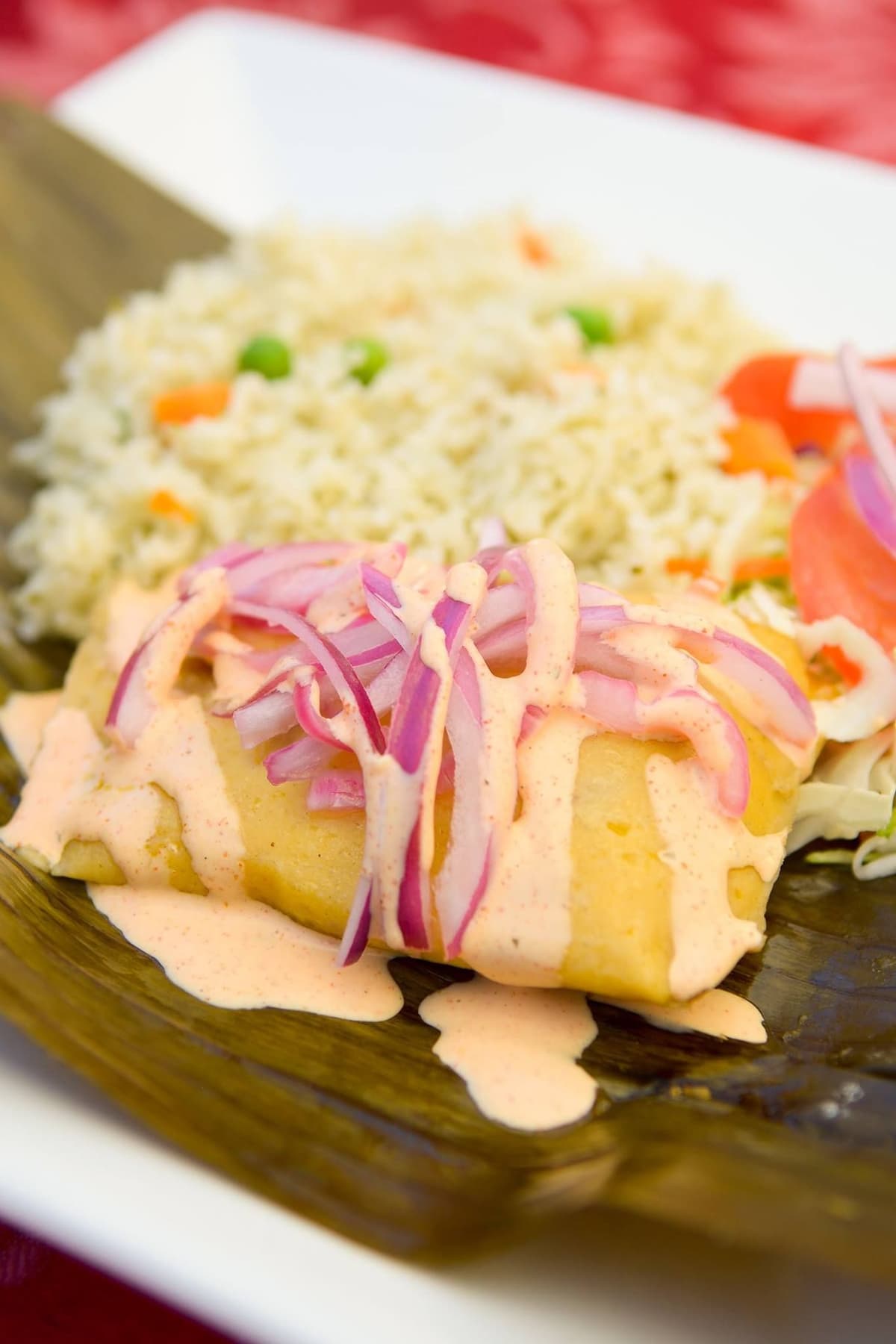 Peruvian corn tamale topped with pickled red onion and aji sauce, a gluten-free office lunch option