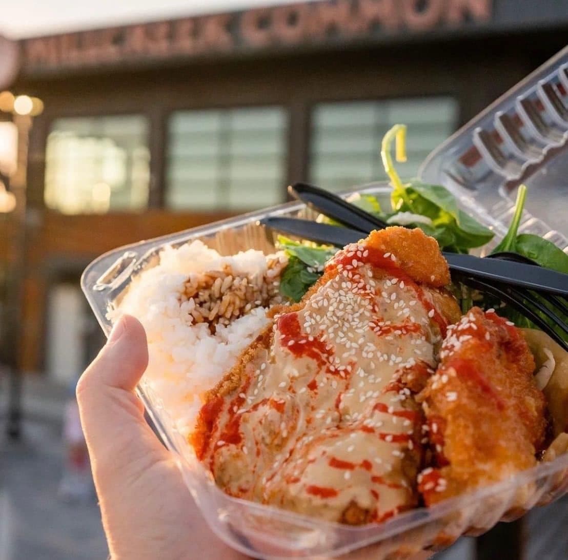 Employee holding a Korean fried chicken rice bowl from a food truck at a corporate catering event