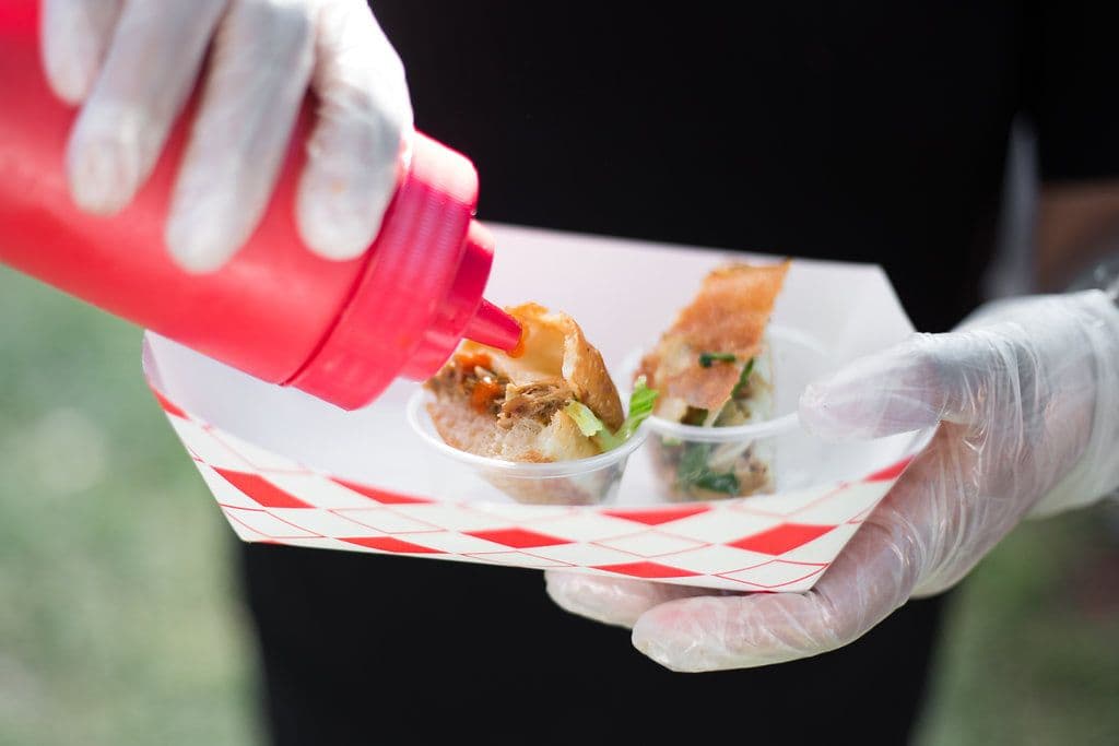 Gloved hands finishing a plated dish with sauce at a corporate food truck catering event
