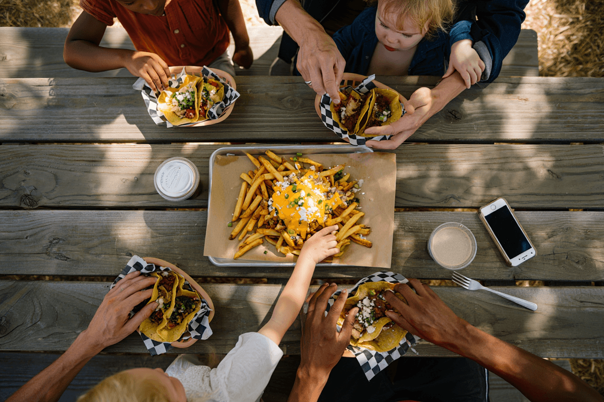 Neighbors sharing a variety of food truck meals at a community picnic table during an HOA food truck night