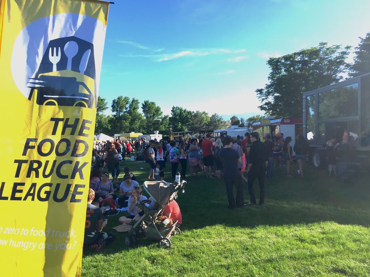 The Food Truck League yellow banner at a crowded outdoor food truck event.